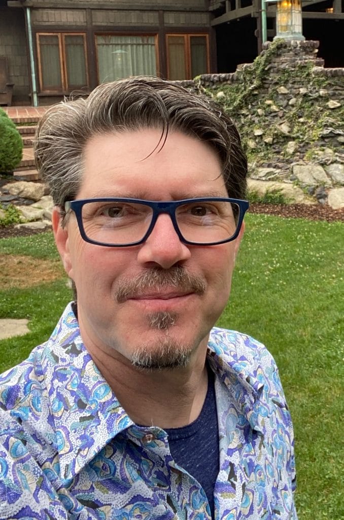 a selfie of Derek Vaughan wearing blue sleeves shirt in front of a house